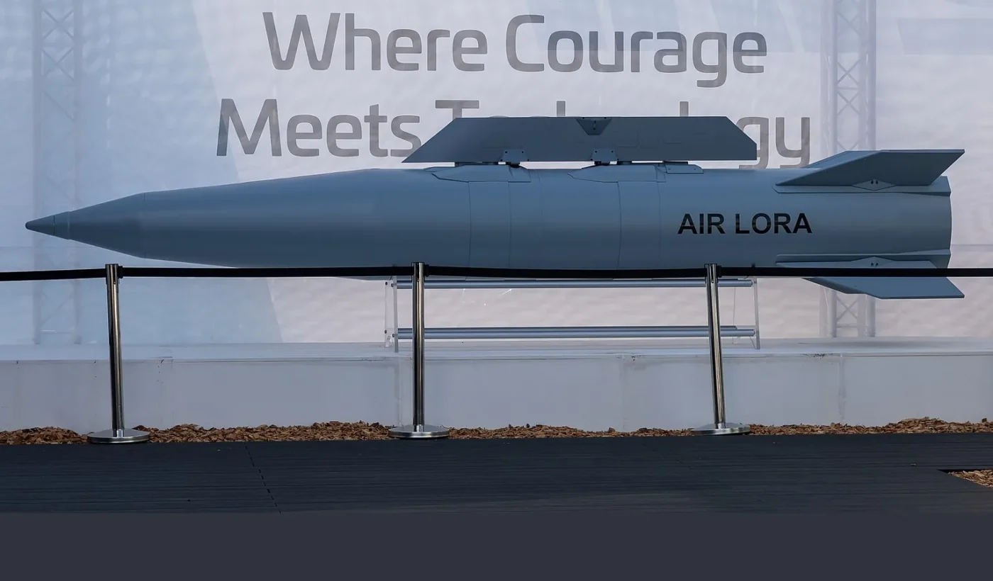 A grey ballistic missile marked AIR LORA displayed on a stand behind a rope barrier