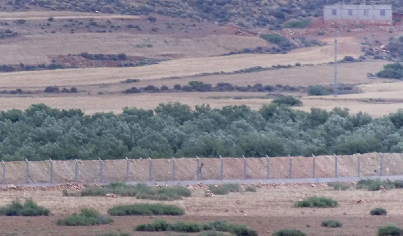 Wire fencing and an earth embankment crossing a dry plain with olive trees on the Moroccan-Algerian border