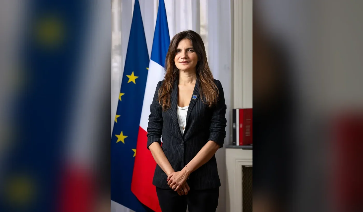Portrait of Alice Rufo standing between a European Union flag and a French flag