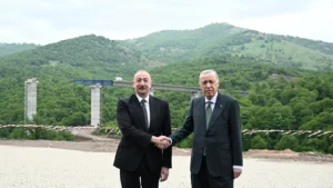 Ilham Aliyev and Recep Tayyip Erdogan shaking hands in front of a highway bridge in a mountainous area