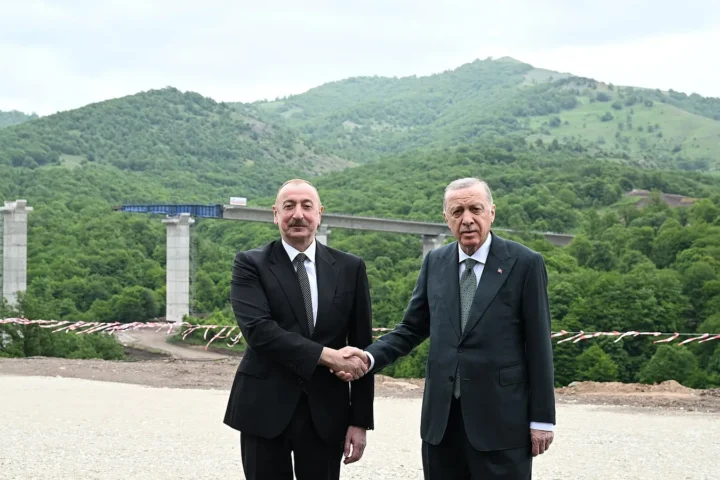 Ilham Aliyev and Recep Tayyip Erdogan shaking hands in front of a highway bridge in a mountainous area