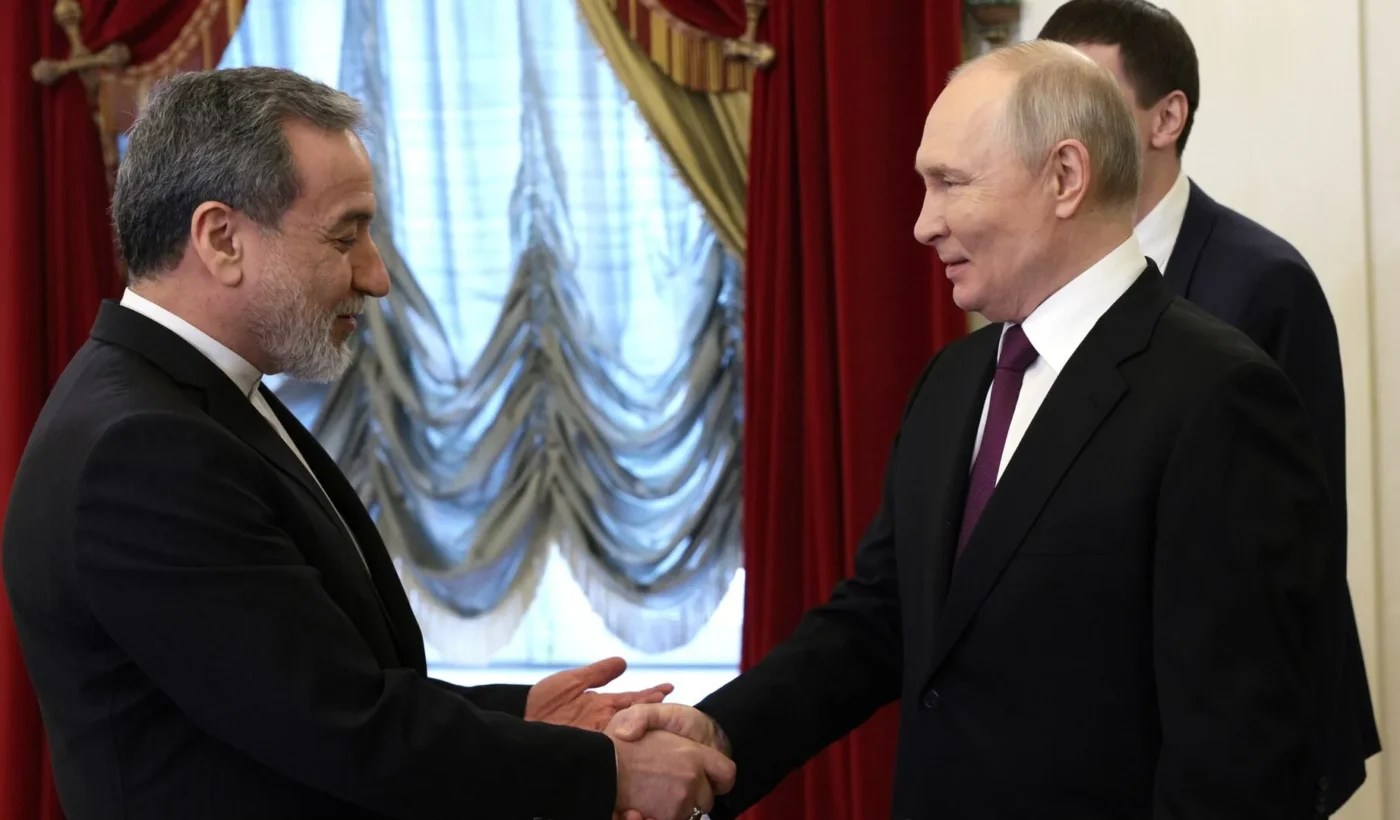 Iranian Foreign Minister Abbas Araghchi shaking hands with Russian President Vladimir Putin in front of red curtains