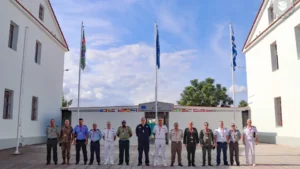Officers of a Hellenic National Defence College delegation stand in front of the EUNAVFOR ASPIDES Operation Headquarters in Larissa, with EU and Greek flags