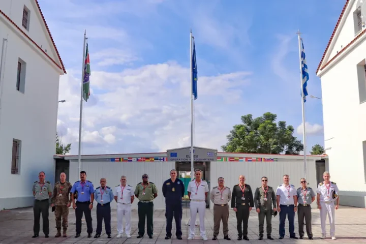 Officers of a Hellenic National Defence College delegation stand in front of the EUNAVFOR ASPIDES Operation Headquarters in Larissa, with EU and Greek flags
