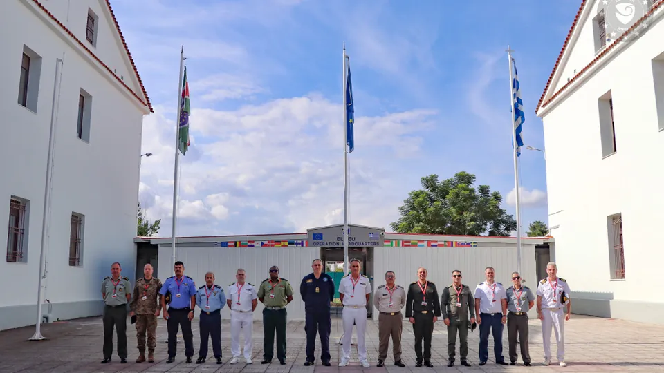 Officers of a Hellenic National Defence College delegation stand in front of the EUNAVFOR ASPIDES Operation Headquarters in Larissa, with EU and Greek flags