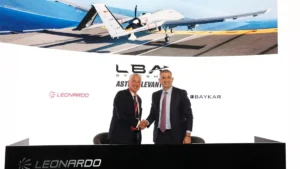 Leonardo and Baykar executives shake hands in front of a display showing the Astore Levante drone on a carrier deck, with the LBA Systems logo