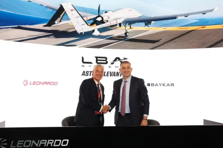 Leonardo and Baykar executives shake hands in front of a display showing the Astore Levante drone on a carrier deck, with the LBA Systems logo