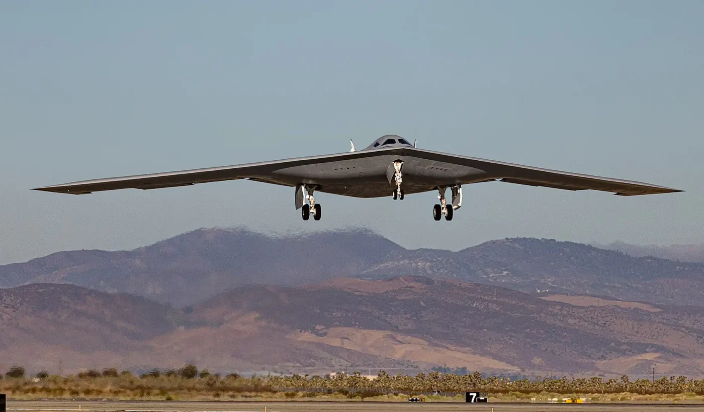 The B-21 Raider stealth bomber seen head-on just after takeoff, with mountains in the background