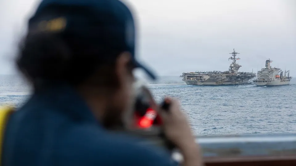 A U.S. Navy sailor aboard USS Spruance looks out at the aircraft carrier USS Abraham Lincoln during a replenishment at sea in the Middle East