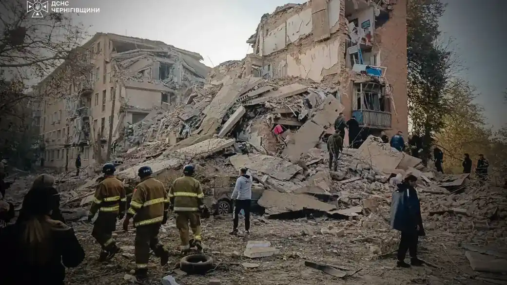 Rescuers and residents stand before the collapsed floors of a five-storey apartment block in Pryluky after a Russian missile strike