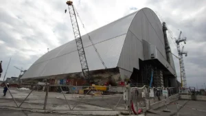 The arched New Safe Confinement over the Chornobyl nuclear power plant, with cranes and fencing in the foreground