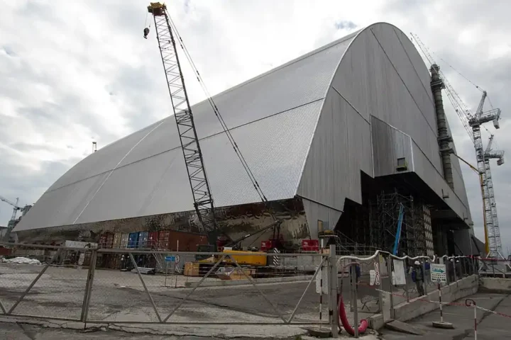 The arched New Safe Confinement over the Chornobyl nuclear power plant, with cranes and fencing in the foreground