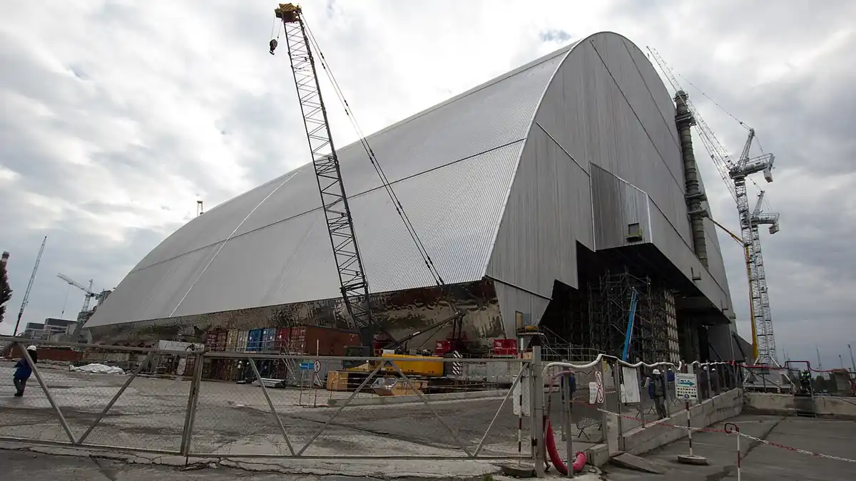 The arched New Safe Confinement over the Chornobyl nuclear power plant, with cranes and fencing in the foreground