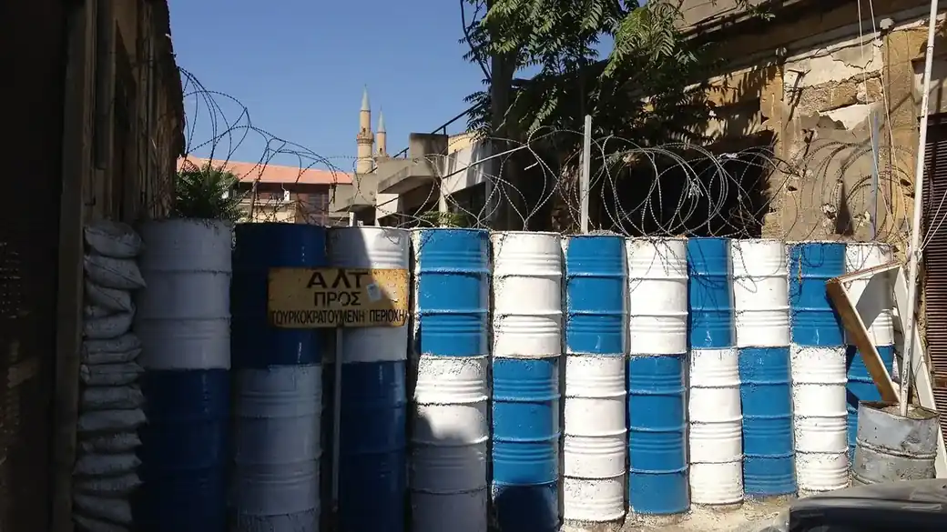Blue and white painted barrels and coils of barbed wire blocking a street in the UN buffer zone in Nicosia, with a sign reading halt