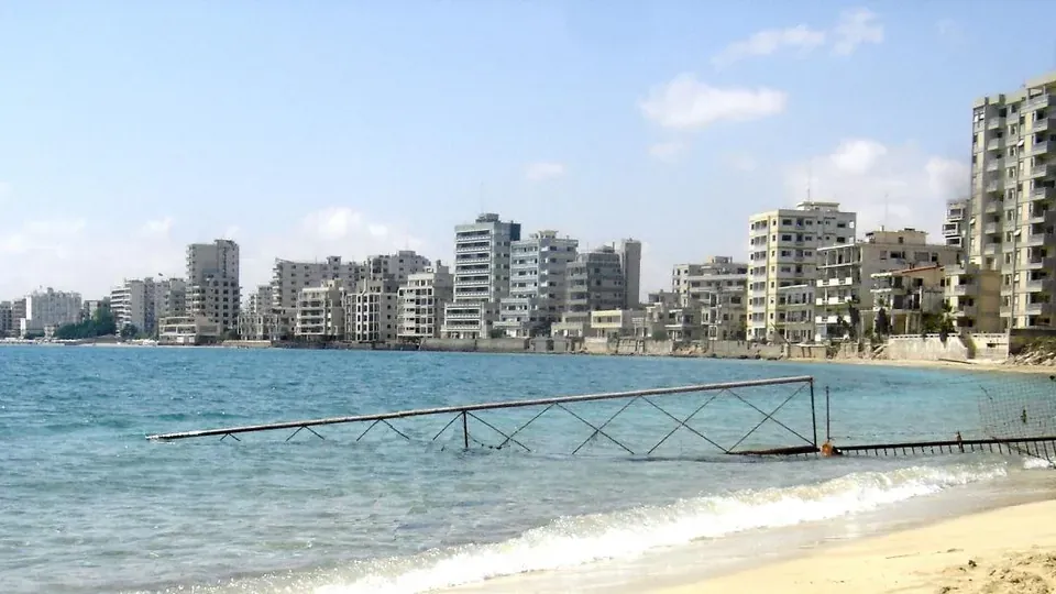 Abandoned high-rise hotels and apartment blocks of Varosha, Famagusta, seen from the beach behind a fence running into the sea