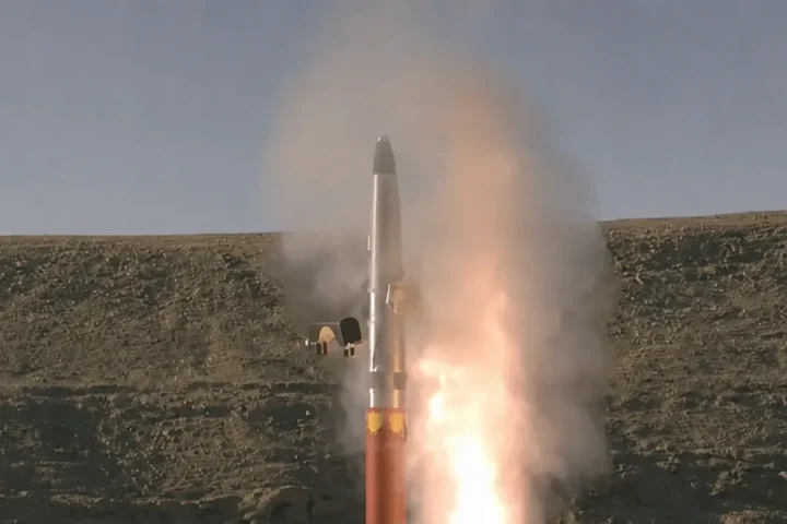 A David’s Sling interceptor missile climbing from its launcher in a plume of smoke and flame against a barren hillside