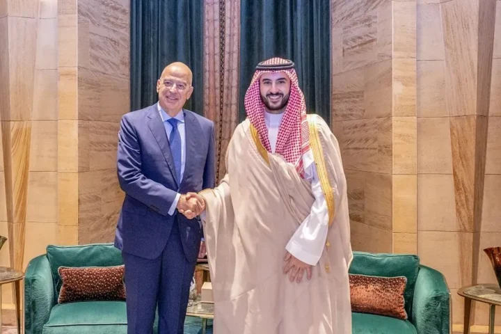Greek Defence Minister Nikos Dendias shakes hands with Saudi Defence Minister Prince Khalid bin Salman in a room with green sofas