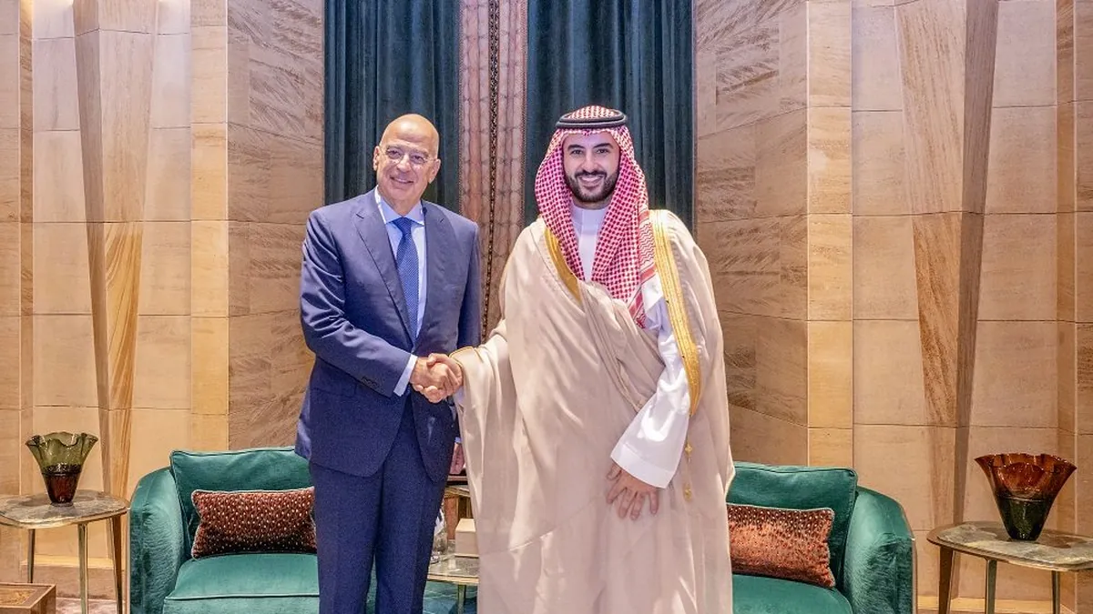 Greek Defence Minister Nikos Dendias shakes hands with Saudi Defence Minister Prince Khalid bin Salman in a room with green sofas