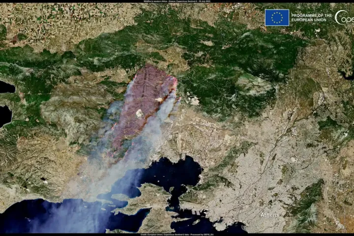 Satellite image of the burn scar and smoke plume of a wildfire in western Attica, with Athens at lower right