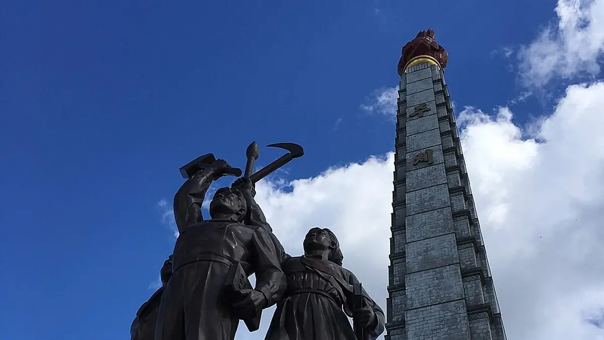 The Juche Tower and a bronze sculpture group in Pyongyang under a blue sky