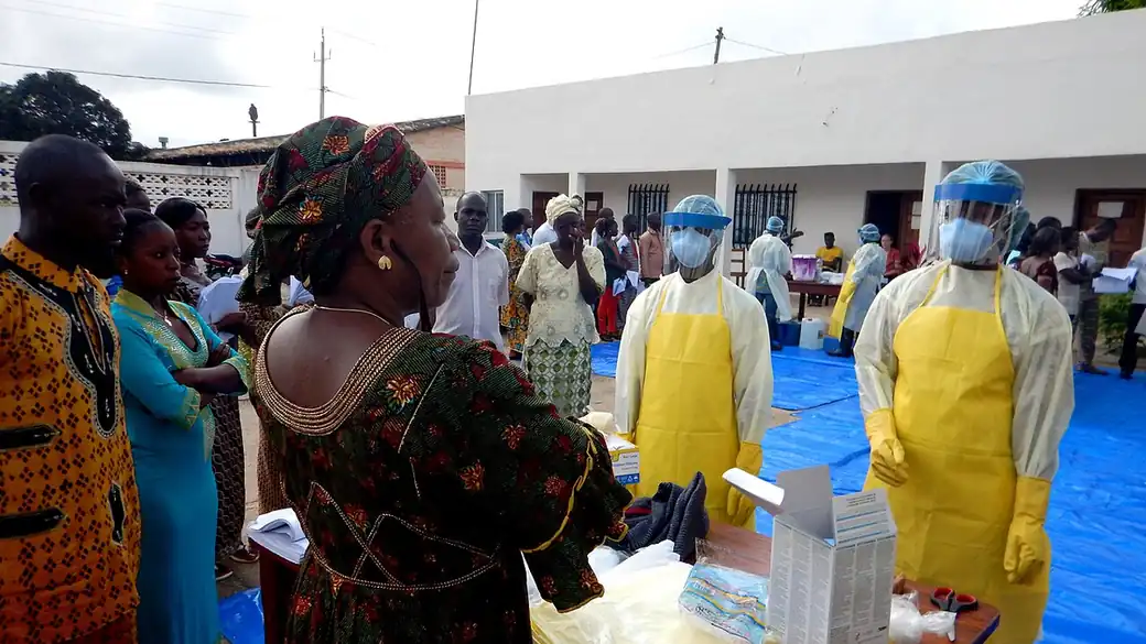 Health workers in yellow aprons, face shields and masks stand beside a table of protective equipment during an Ebola response training session in Guinea