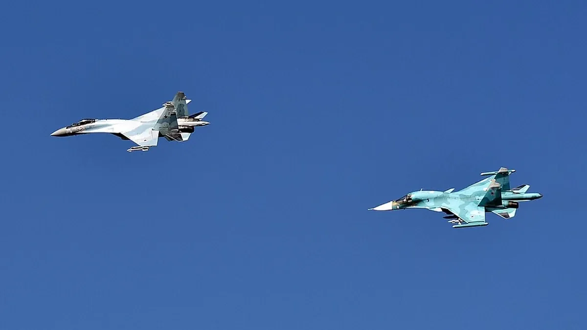 A Russian Su-35S fighter (left) and a Su-34 fighter-bomber flying together against a blue sky