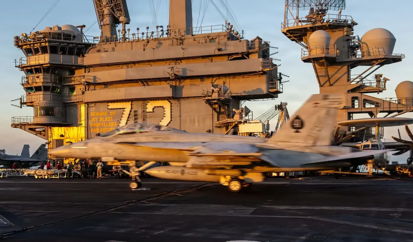 An F/A-18F Super Hornet moving across the flight deck of USS Abraham Lincoln in warm evening light, with the island marked 72 behind it