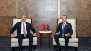 Turkish Foreign Minister Hakan Fidan seated beside another minister at a bilateral meeting, with small Turkish and Azerbaijani flags between them