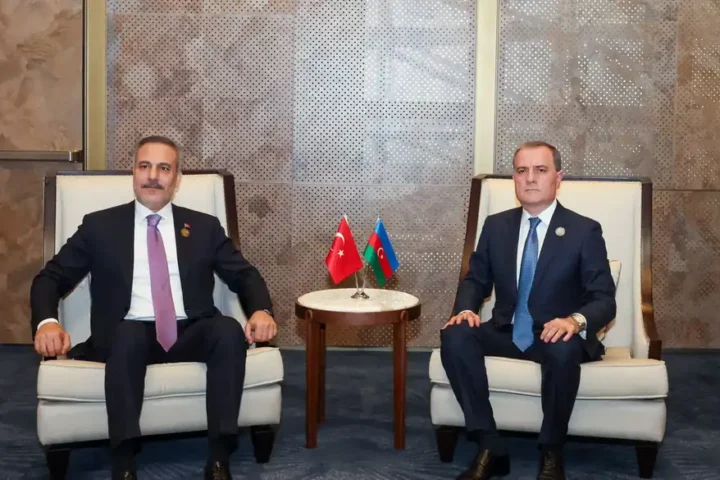 Turkish Foreign Minister Hakan Fidan seated beside another minister at a bilateral meeting, with small Turkish and Azerbaijani flags between them
