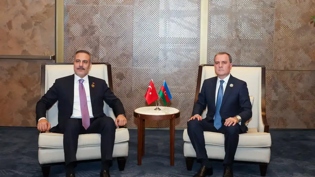 Turkish Foreign Minister Hakan Fidan seated beside another minister at a bilateral meeting, with small Turkish and Azerbaijani flags between them
