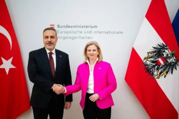 Turkish Foreign Minister Hakan Fidan shaking hands with Austrian Foreign Minister Beate Meinl-Reisinger in Vienna, with Turkish, Austrian and EU flags