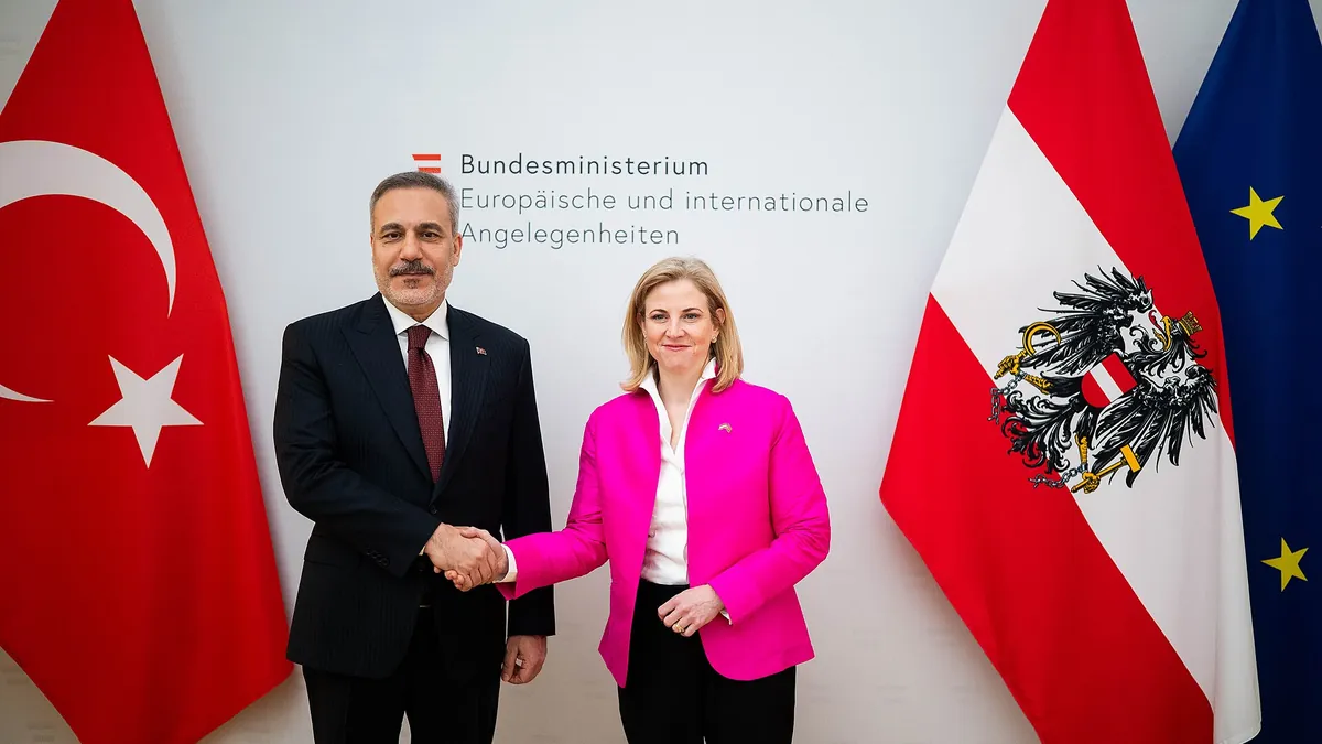 Turkish Foreign Minister Hakan Fidan shaking hands with Austrian Foreign Minister Beate Meinl-Reisinger in Vienna, with Turkish, Austrian and EU flags