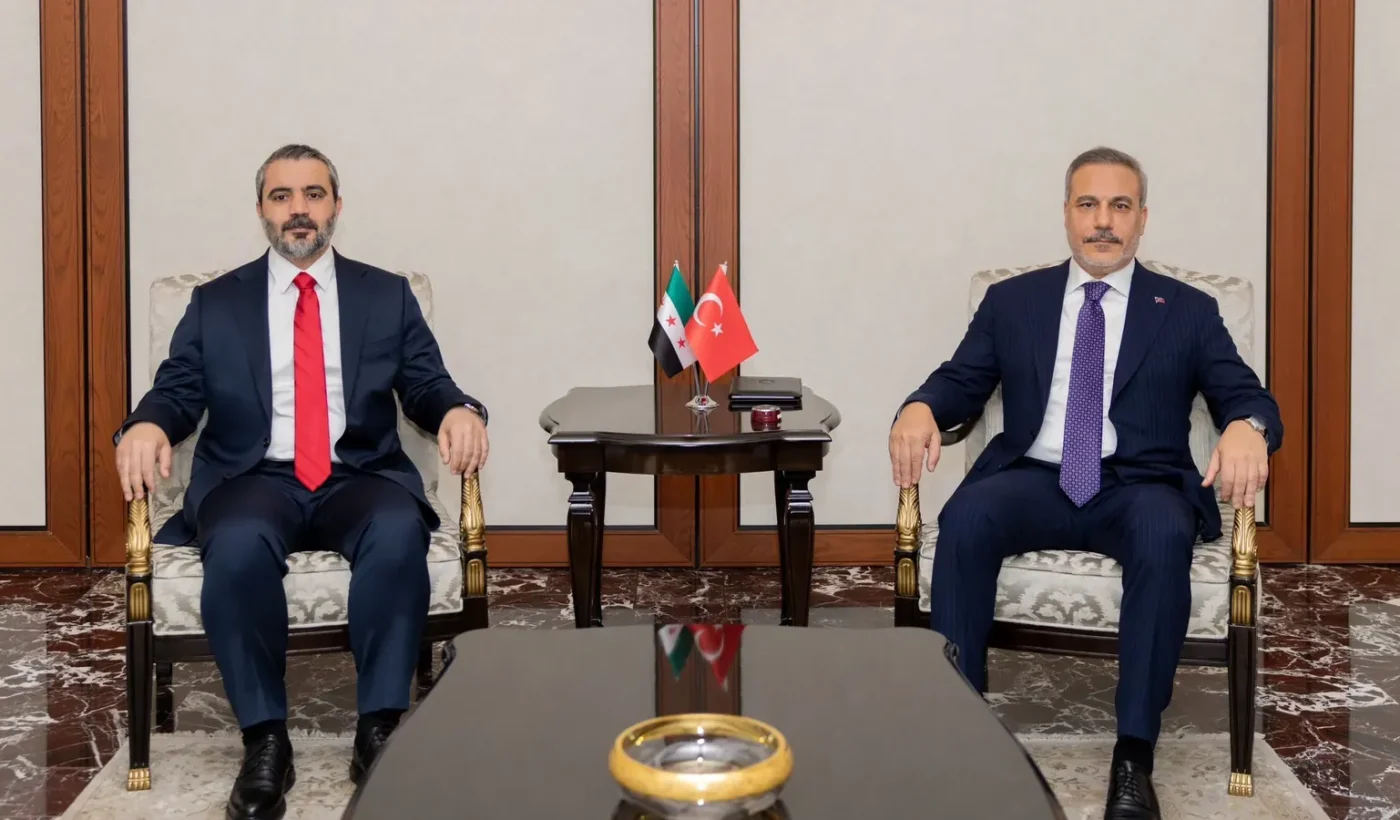 Turkish Foreign Minister Hakan Fidan and Syrian Foreign Minister Asaad al-Shaibani seated in armchairs in front of the flags of Turkey and Syria