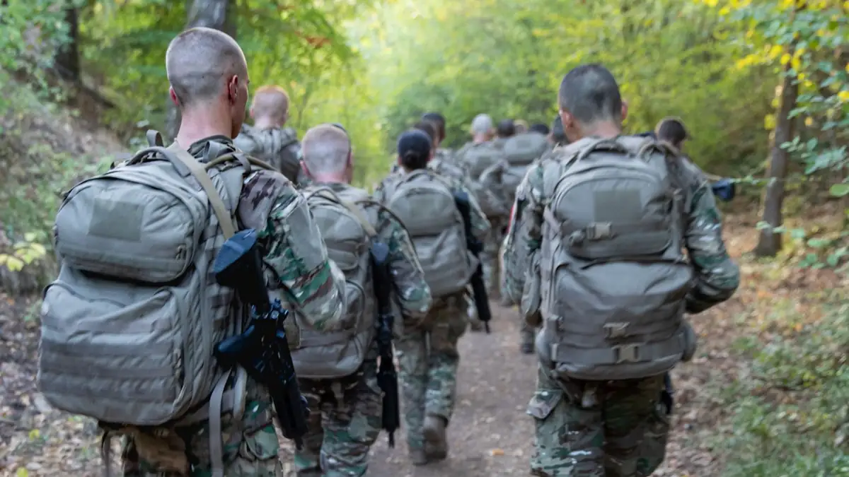 Young French national service recruits in camouflage with backpacks marching in a column along a forest path