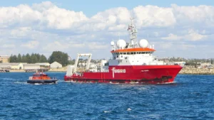 A white and orange research vessel leaving a harbour