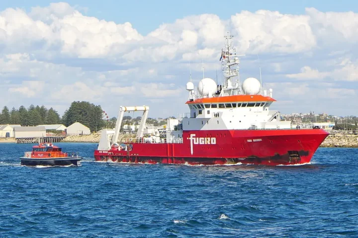 A white and orange research vessel leaving a harbour