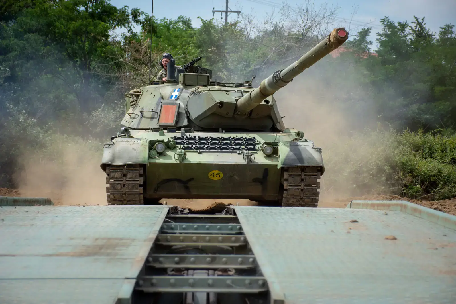 A Hellenic Army Leopard 1A5 tank with the Greek flag on its turret crossing a bridging platform