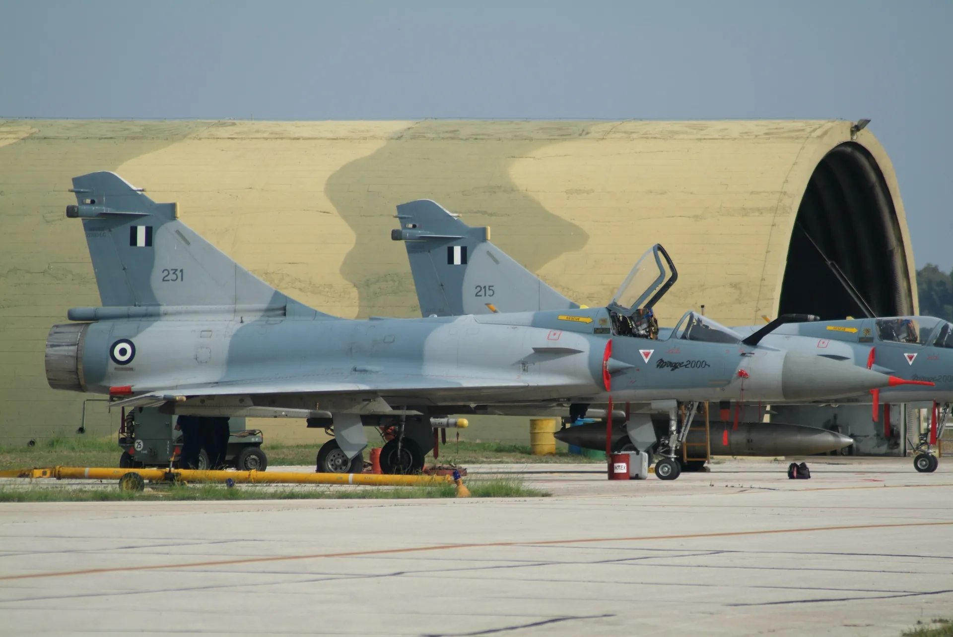 Two Hellenic Air Force Mirage 2000EG, numbers 231 and 215, in front of a hardened aircraft shelter