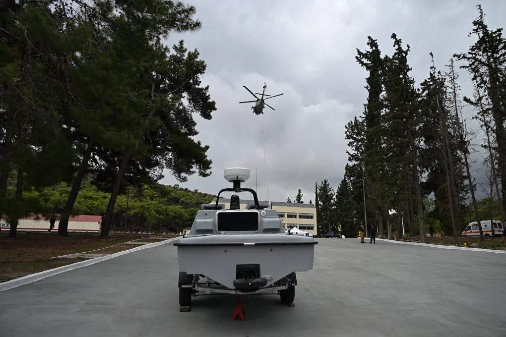 The grey Pyrpolitis unmanned surface vessel on a trailer, seen from the front, with a helicopter flying overhead