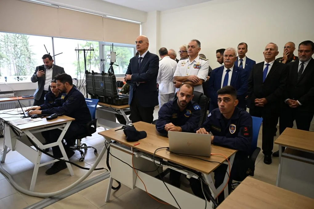 Navy personnel working at computers while the minister and officers watch