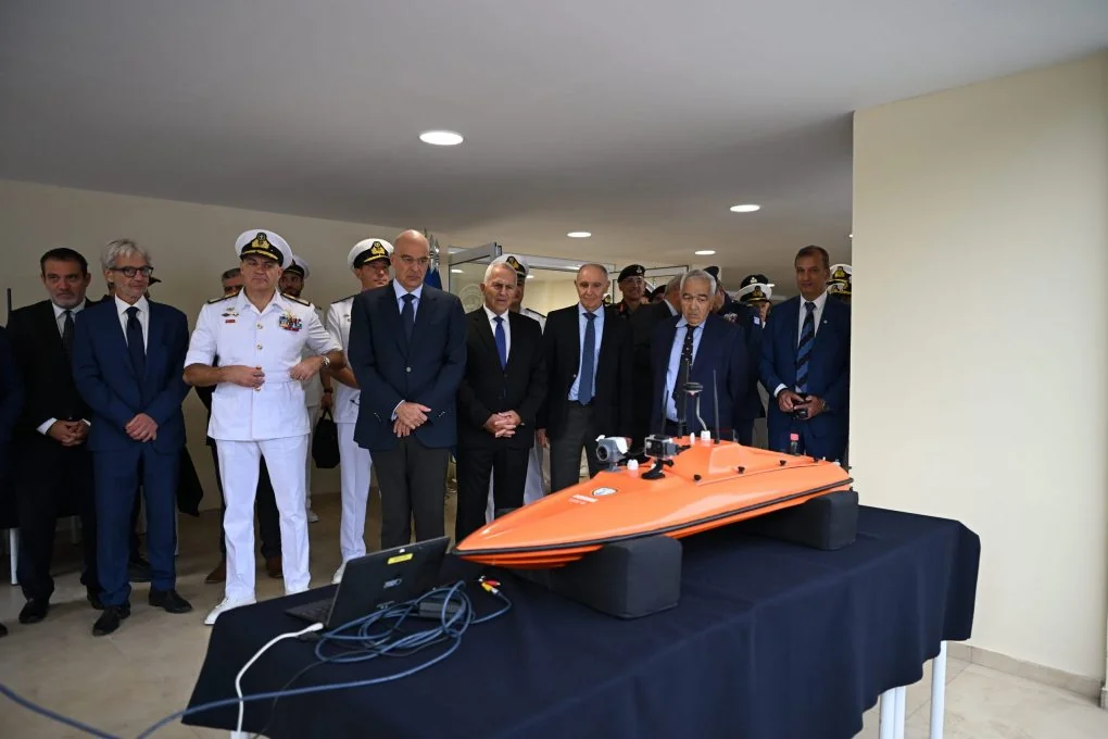 Nikos Dendias, the Navy chief and guests in front of a small orange unmanned vessel with cameras