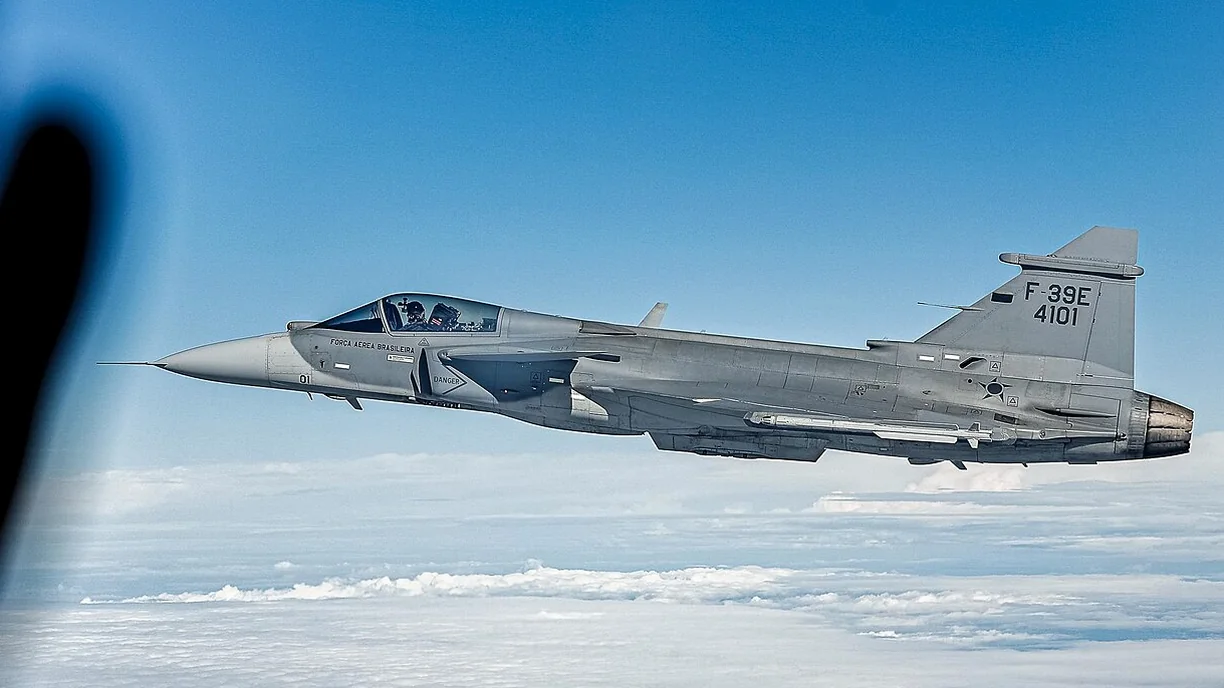 A Brazilian Air Force F-39E Gripen, serial 4101, flying above clouds under a blue sky