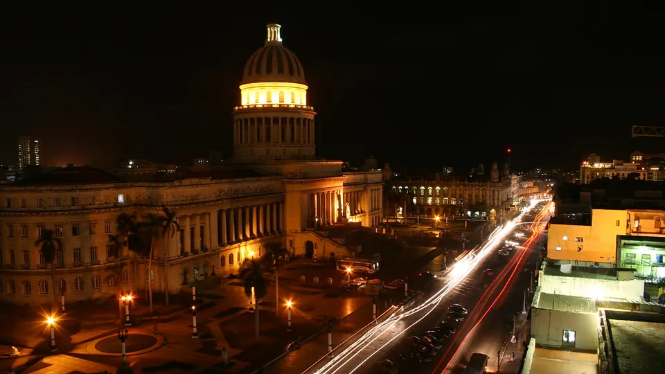 The illuminated dome of El Capitolio in Havana at night, with light trails from traffic on the street beside it