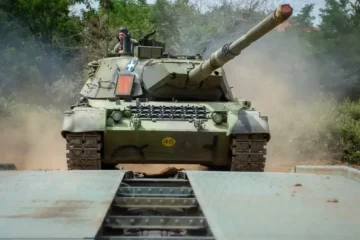 A Hellenic Army Leopard 1A5 tank with the Greek flag on its turret crossing a bridging platform