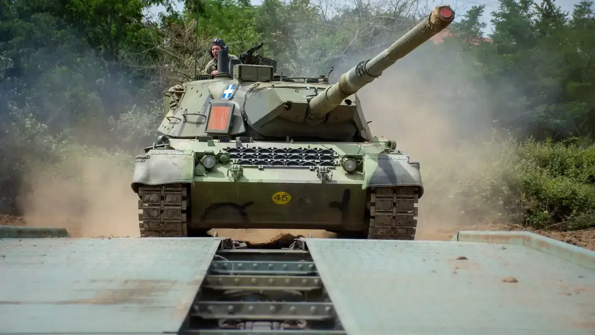 A Hellenic Army Leopard 1A5 tank with the Greek flag on its turret crossing a bridging platform