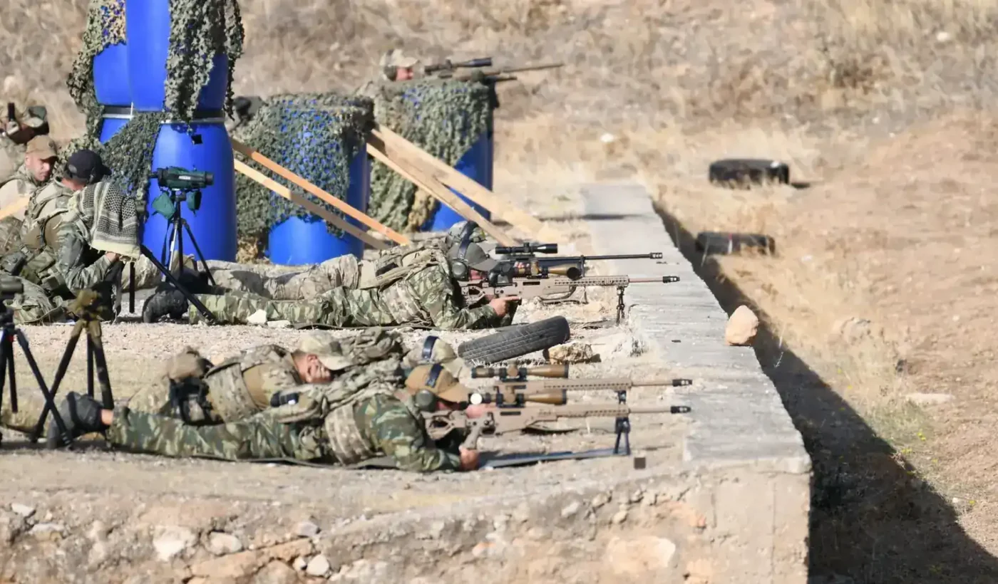 Greek Armed Forces snipers lying in the prone position with sniper rifles on a firing range, with spotters and spotting scopes beside them