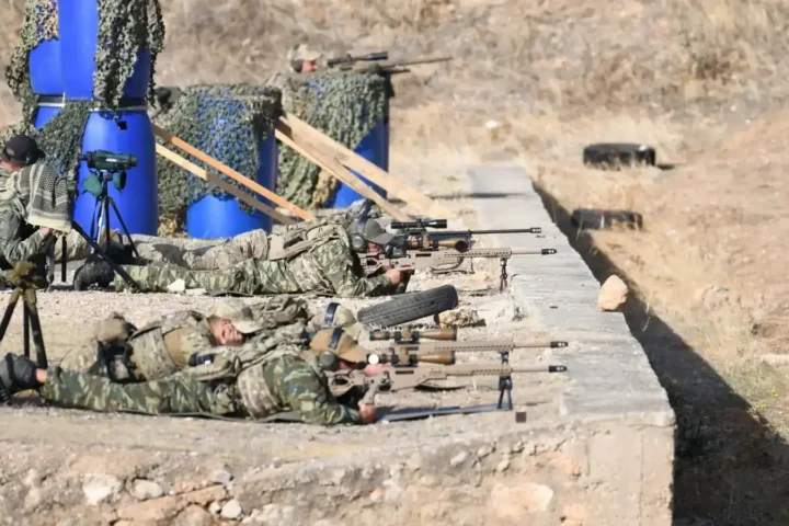 Greek Armed Forces snipers lying in the prone position with sniper rifles on a firing range, with spotters and spotting scopes beside them
