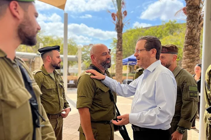 The Israeli president in a white shirt embraces a soldier among soldiers in khaki uniforms at a base