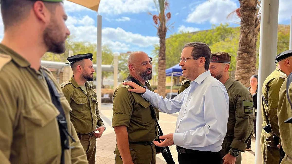 The Israeli president in a white shirt embraces a soldier among soldiers in khaki uniforms at a base