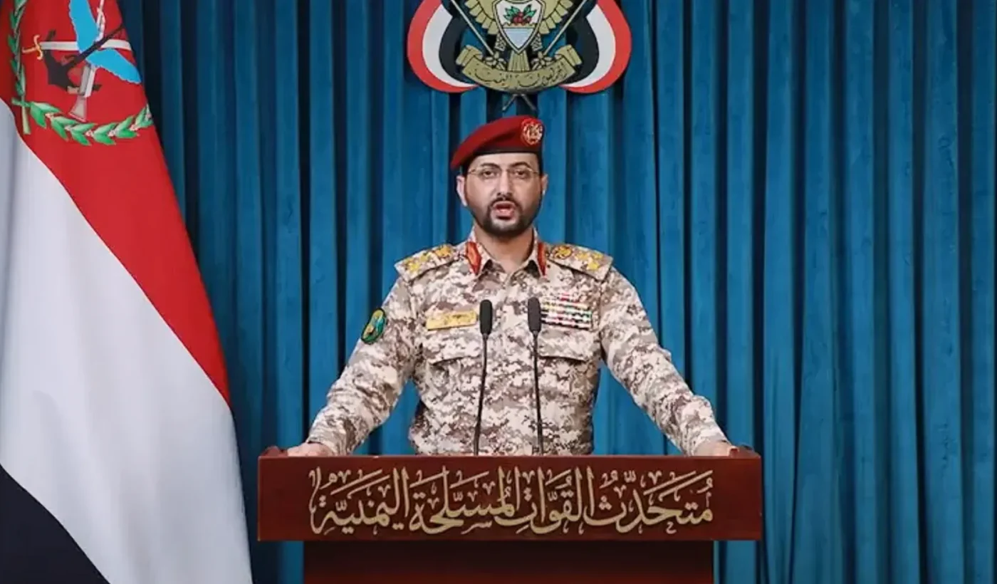 A Houthi military spokesman at a podium in front of Yemeni flags